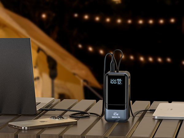 A compact, multi-functional USB-C hub with charging capabilities, surrounded by a laptop and other devices in a cozy, dimly lit workspace.